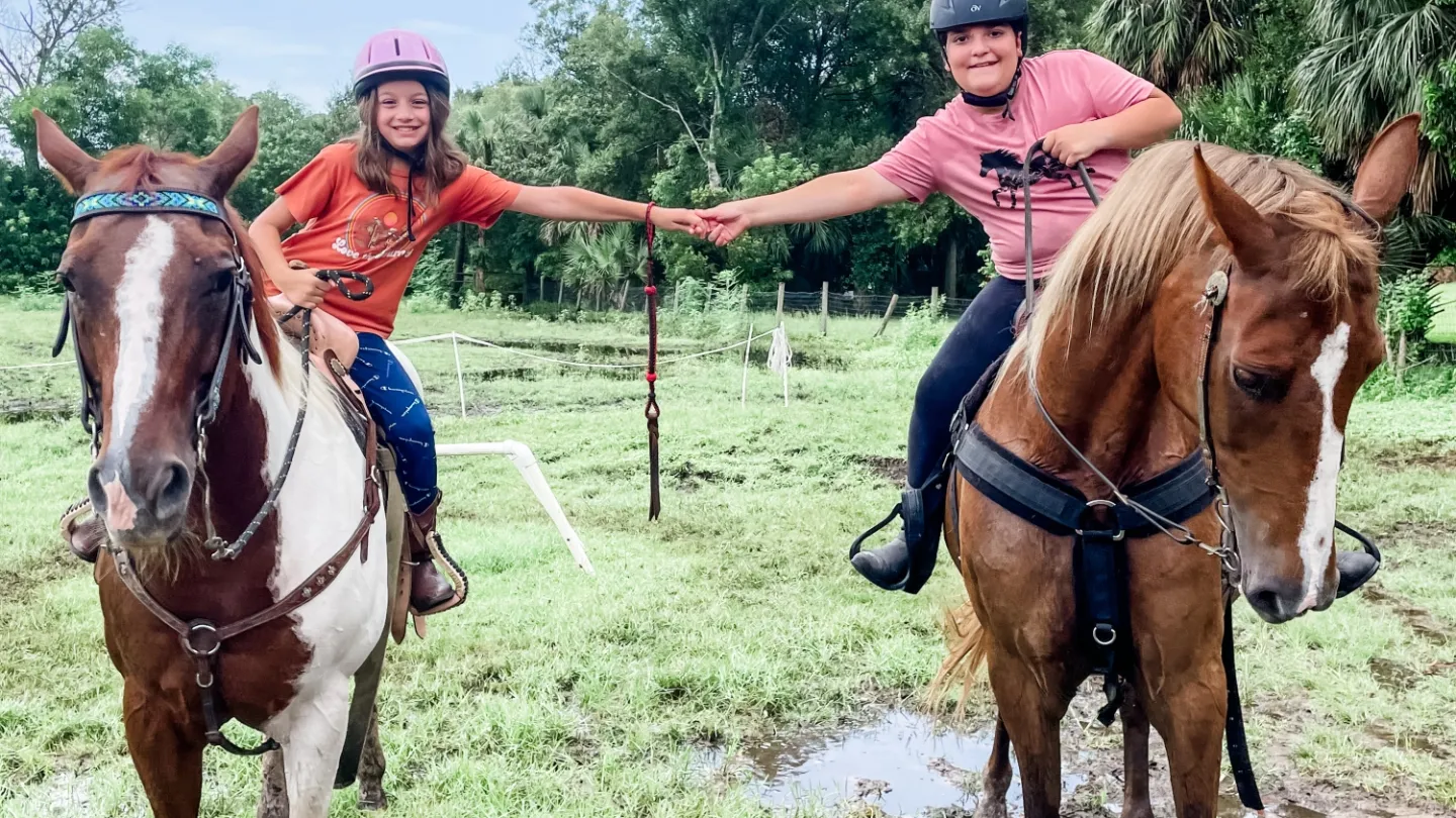 \Two girls horseback riding on a wooded trail during Equestrian Day at Jupiter Outdoor Center’s summer camp